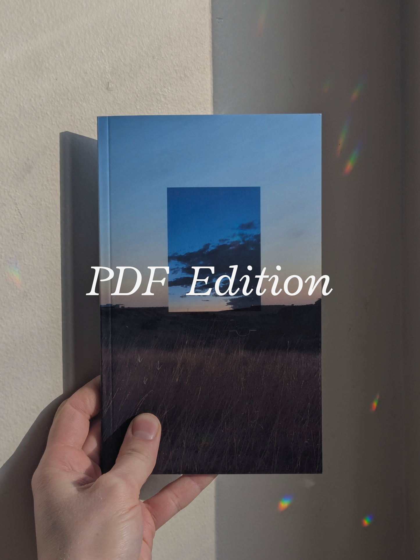 Book featuring a cover of a field, a blue sky, and clouds, held by a hand against a neutral background with refracted light. Across the image text reads "PDF Edition."